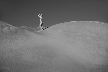 Genç bir kadın kumlu dağda elbise giymiş poz veriyor.