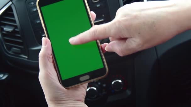 Close-up van een vrouwenhand met een mobiele telefoon met een verticaal groen scherm in een auto. — Stockvideo