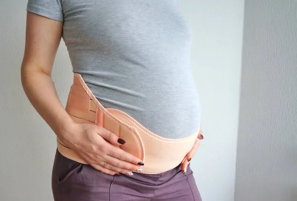 怀孕妇女的绷带 一个孕妇穿着紧身衣来支撑她的胃和背痛 女孩用双手托住怀孕的肚子 并戴上绷带 图库图片