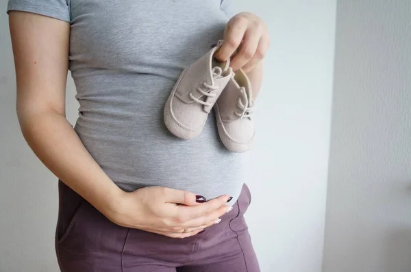 Una Chica Embarazada Toca Vientre Sostiene Los Zapatos Bebé Esperando — Foto de Stock