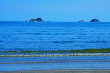 Önünde ve dışında küçük dalgalar olan mavi deniz ve mavi gökyüzünde bir yelkenli tekne.
