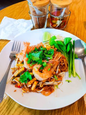 Tahta masadaki beyaz tabakta sebzeli Tayland usulü erişte.