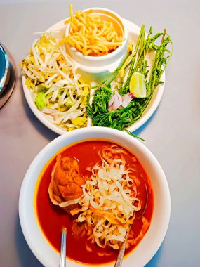 Northern Thai curry noodle in white bowl and fresh vegetables beside