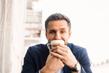 Adam kahveyi seviyor. Kafede bir fincan kahveyle yakışıklı bir adam. Erkeğin sabah yaşam tarzı. Adam yazlık terasta oturmuş kahve içiyor ve gülümsüyor.