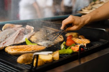 Somon, levrek ve sebze karışımı deniz ürünleri pişirmek. Acılı patates ve domatesli ızgara balık.