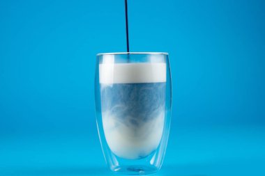 Çift cam bardakta mavi anchan matcha latte. Mavi arkaplanda kibrit kokteyli