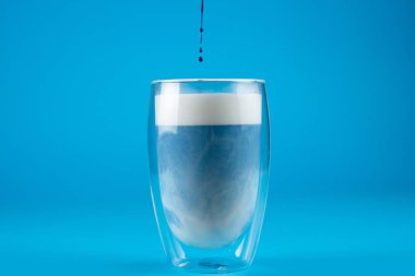 Çift cam bardakta mavi anchan matcha latte. Mavi arkaplanda kibrit kokteyli