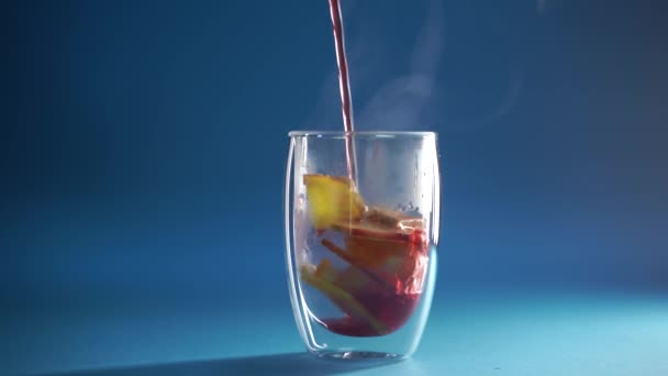 4k video pouring mulled red wine in double glass cup on blue background. Alcohol punch Drink with orange, anise star, cinnamon and apple. — Stock Video