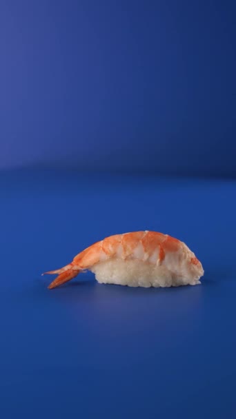 Nigiri crevettes sushi filant sur fond bleu. Vidéo alimentaire verticale Sushi 4k pour les réseaux sociaux. — Video