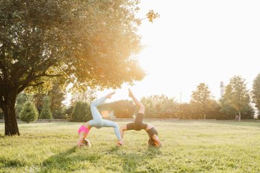2 kız parkta spor antrenmanı ve yoga yapıyor.