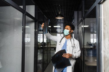 Afrikalı doktor bir klinikte röntgenleri inceliyor. Tıp maskeli siyahi öğrenci tomografilere bakıyor.