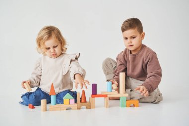 Çocuk, beyaz arka planda oyuncak tahta küpleri olan neşeli bir çocukla oynuyor. Çocuklar gülümser ve birlikte eğlenirler.