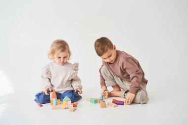 Çocuk, beyaz arka planda oyuncak tahta küpleri olan neşeli bir çocukla oynuyor. Çocuklar gülümser ve birlikte eğlenirler.