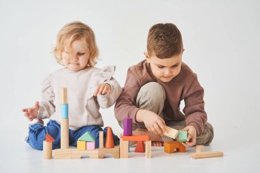 Erkek ve kız bebek gülümsüyor, eğleniyor ve beyaz arka planda renkli tuğlalarla oynuyor. Çocuklar gülümser ve birlikte eğlenirler.