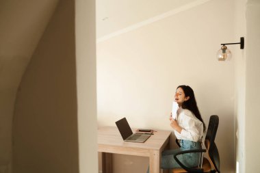 Öğrenci kız sınavı geçti ve yüksek notla seviniyor. Çevrimiçi eğitim ve uzaktan öğrenme. Dizüstü bilgisayarı olan kadın elinde sınav sonuçları olan kağıtlar tutuyor ve seviniyor.