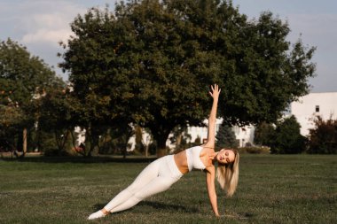Parktaki çimlerin üzerinde esneme antrenmanı. Açık hava antrenmanından önce sarışının ısınması. Spor yaşam tarzı