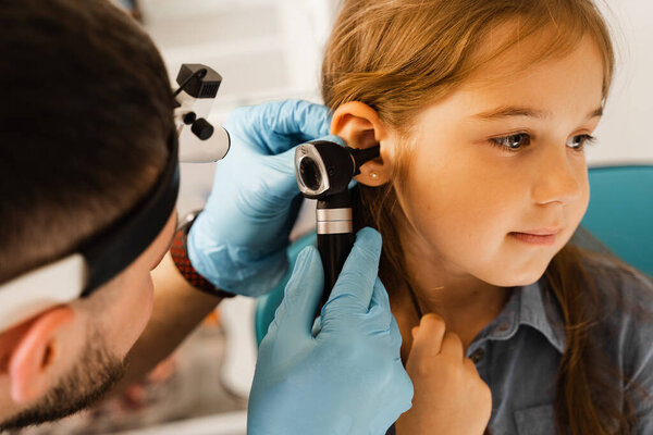 ENT doctor otolaryngologist looks through otoscope the ears of a little girl. Otoscopy. Treatment child ear pain