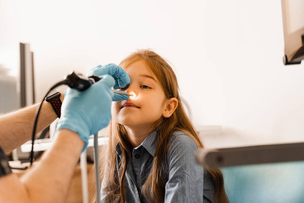 Nose endoscopy of child. Rhinoscopy procedure with rhinoscope. ENT doctor otolaryngologist with headlight treat nose kid patient