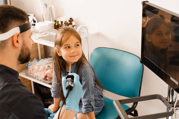 Nose endoscopy of child. Rhinoscopy procedure with rhinoscope. ENT doctor otolaryngologist with headlight treat nose kid patient