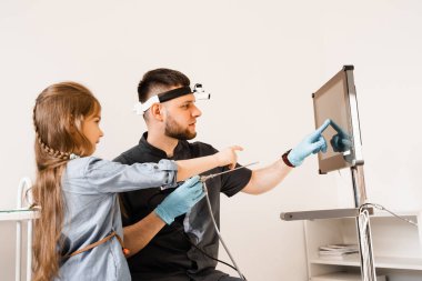 KBB doktoru otolarosengolog çocuk endoskopisi ve otoskopi için farları gösteriyor. Çocuğun burun ve kulakları endoskopisi