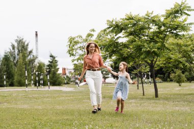 Anne ve kızı parkta koşup eğleniyorlar. Aile değerleri ve gelenekler. Mutlu bir çocukluk dönemi. Anne kızıyla oynuyor.