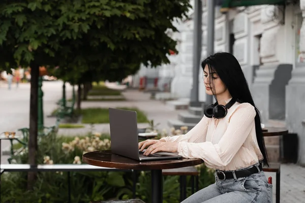 Woman with vitiligo skin pigmentation on the hands working on laptop online and listen music with headphones outdoor in cafe. Skin seasonal disease