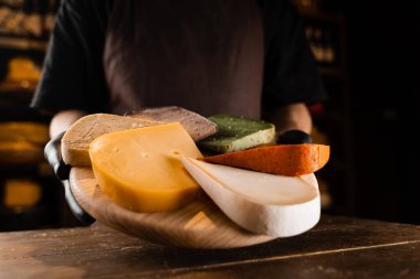 Masada taze Gouda, genç keçi, lavanta peyniri, yeşil ve kırmızı pesto peyniri karışımı peynir tabağı tutan peynir. Peynir dükkanı reklamı için yaratıcı bir fikir.