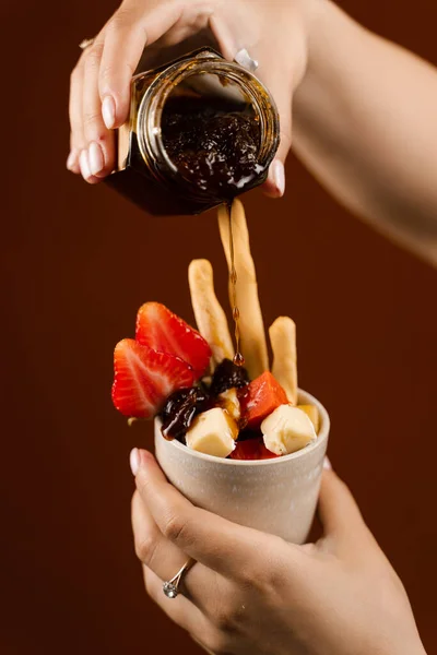 Pouring jam on mix of cheeses, grissini chopsticks and strawberry in cup. Creative idea for advertising a cheese shop