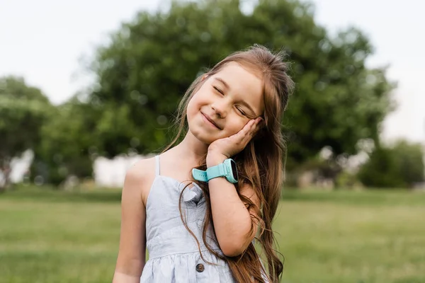 Delikatna Dziewczynka Dotykająca Policzka Uśmiechnięta Uroczy Dzieciak Pozujący Zewnątrz Parku — Zdjęcie stockowe
