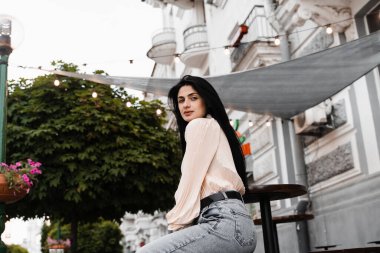 Sevimli Gürcü kadın açık kafede oturuyor ve poz veriyor. Farklı duyguları olan moda kızı yaz terasında siparişini bekliyor.