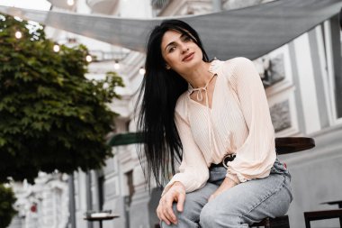 Sevimli Gürcü kadın açık kafede oturuyor ve poz veriyor. Farklı duyguları olan moda kızı yaz terasında siparişini bekliyor.