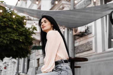 Sevimli Gürcü kadın açık kafede oturuyor ve poz veriyor. Farklı duyguları olan moda kızı yaz terasında siparişini bekliyor.