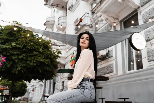 Sevimli Gürcü kadın açık kafede oturuyor ve poz veriyor. Farklı duyguları olan moda kızı yaz terasında siparişini bekliyor.