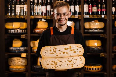 Yakışıklı peynir sommelieri ve 2 parça sarı peynir tekeri, doğal yaşlanma sınırını zorluyor. Peynir doğrama mağazasında. Ellerinde büyük peynir parçaları