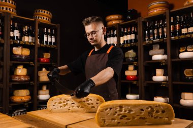 Peynir dükkanında çalışan yakışıklı bir adam bıçakla sınırlandırılmış maasdam doğasını kesti. Peynir dükkanında çalışan peynirli şarap garsonu. Peynir reklamları için yaratıcı fikirler