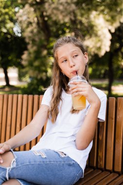 Yaz limonatası içen çekici bir kız çocuğu. Yaz kokteylleri. Portakallı limonata bardağı tutan mutlu kız.