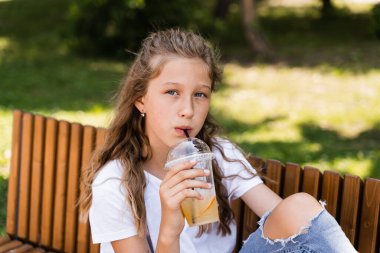 Yaz limonatası içen çekici bir kız çocuğu. Yaz kokteylleri. Portakallı limonata bardağı tutan mutlu kız.