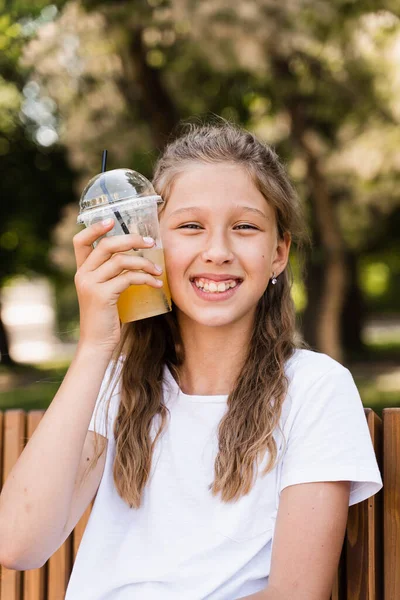 Summer lemonade cocktail outdoor. Happy girl holding cup with orange lemonade and smiling and laughing