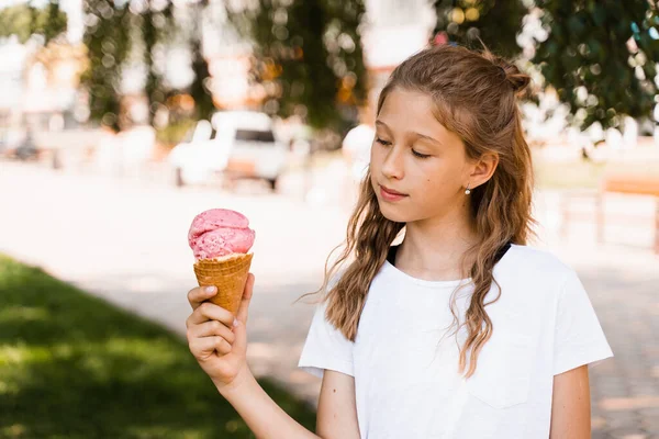 Happy child girl with ice cream cone in summer park. Attractive girl holding sweets ice cream cone and smiling