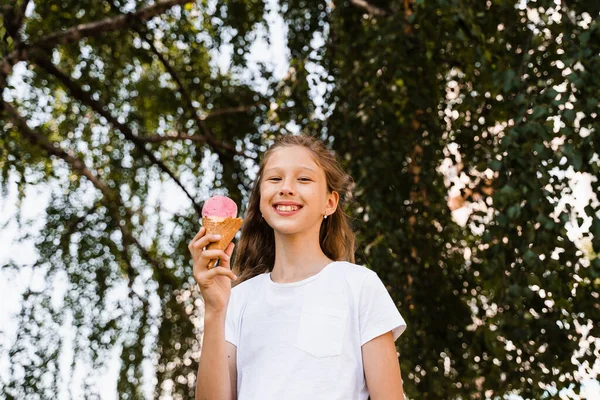 Happy child girl with ice cream cone in summer park. Attractive girl holding sweets ice cream cone and smiling