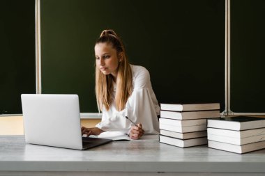 Eğitim. Dizüstü bilgisayarda daktilo kullanan ve okul yönetiminde internetten ders çalışan kız öğrenci. Okula dönelim. Kitapları olan kız tahtada online çalışıyor.