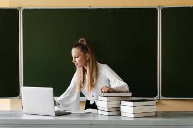 Eğitim. Dizüstü bilgisayarda daktilo kullanan ve okul yönetiminde internetten ders çalışan kız öğrenci. Okula dönelim. Kitapları olan kız tahtada online çalışıyor.