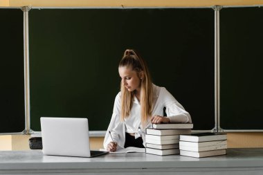Eğitim. Dizüstü bilgisayarda daktilo kullanan ve okul yönetiminde internetten ders çalışan kız öğrenci. Okula dönelim. Kitapları olan kız tahtada online çalışıyor.