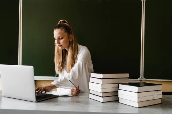 Education. Schoolgirl typing on laptop and study online at school board. Back to school. Girl with books studying online at blackboard