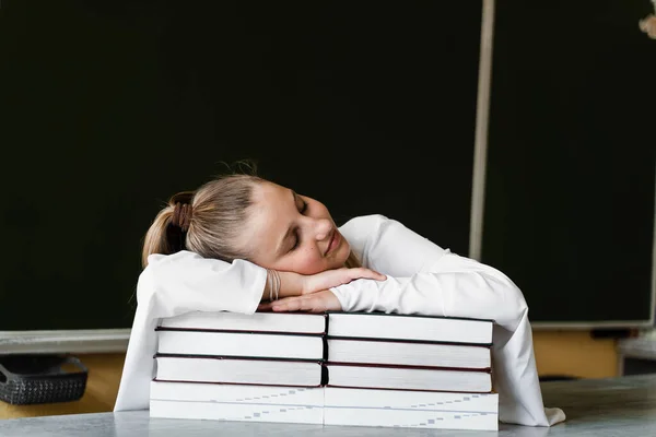 Tired schoolgirl lies and sleeping on books at blackboard in school. School education. The girl is tired of teaching homework