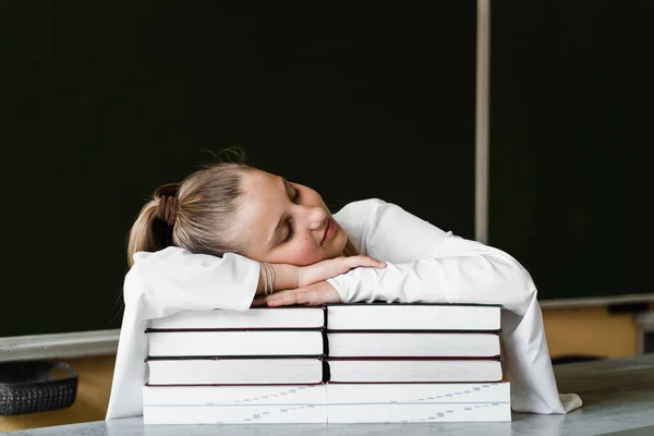 Tired schoolgirl lies and sleeping on books at blackboard in school. School education. The girl is tired of teaching homework