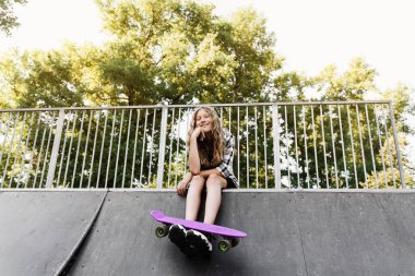 Kaykay sporu rampasında oturan kaykaylı aktif bir çocuk. Ekstrem spor yaşam tarzı. Spor çocuk mağazası için yaratıcı reklam