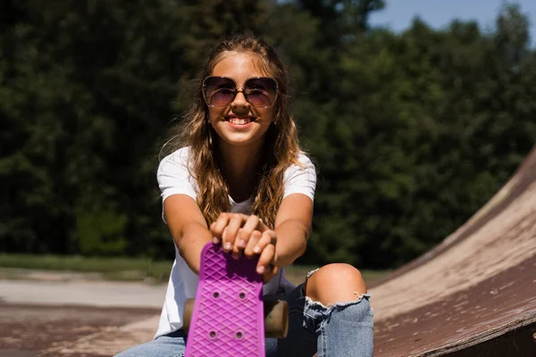 Happy smiling girl with skate board sitting on skate playground and having fun. Extreme sport lifestyle. Laughing child with skate board posing on sport ramp