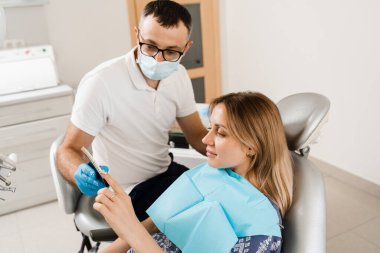 Diş hekimi, diş sağlığı kliniğindeki kadın hastalara diş beyazlatma için diş tonu rehberliği gösteriyor. Diş hekimliği. Kadın kaplamalara bakıyor ya da diş implantı yerleştiriyor. Diş renkleri doktorun ellerinde eşleşiyor.