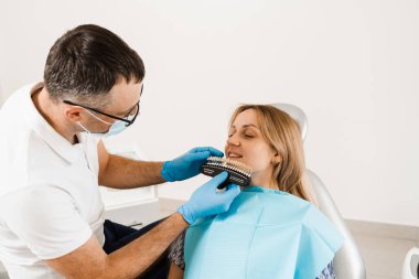 Diş beyazlatma. Diş hekimi, diş tonu rehberiyle çalışıyor. Diş hekimliği. Doktor diş sağlığı kliniğinde diş rengine uyan örnekleri kontrol ediyor.